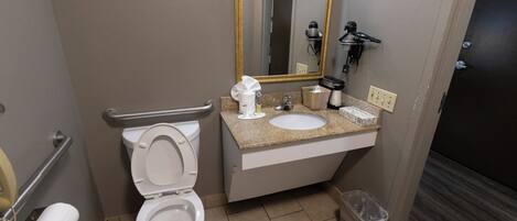 A bathroom with a toilet, sink, mirror, and hand dryer.