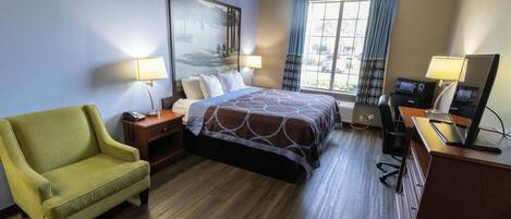 Habitación de hotel con cama, escritorio con computadora, silla, lámpara de escritorio y ventana con cortinas.