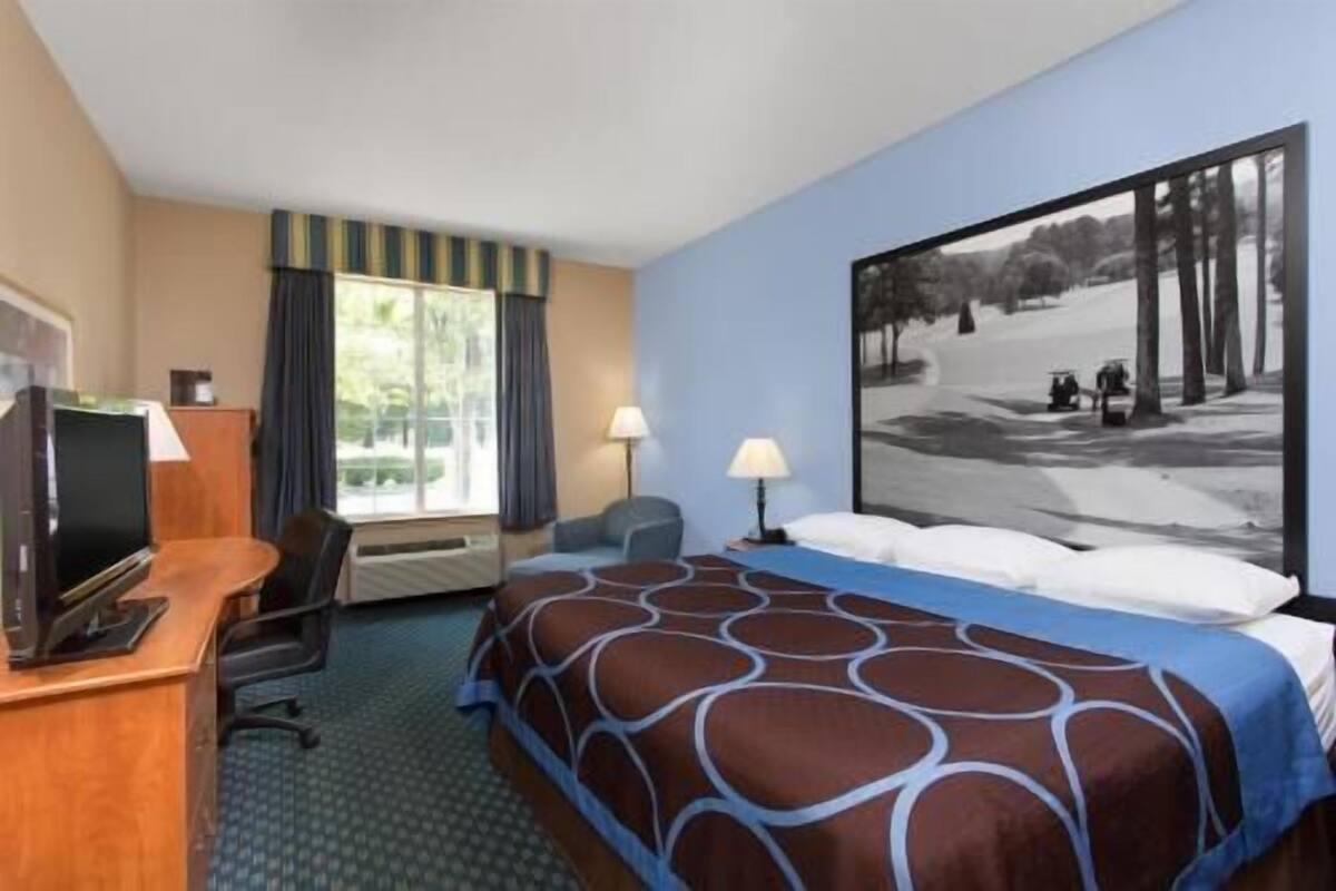 Una habitación de hotel con cama, escritorio, silla y un ventanal grande.