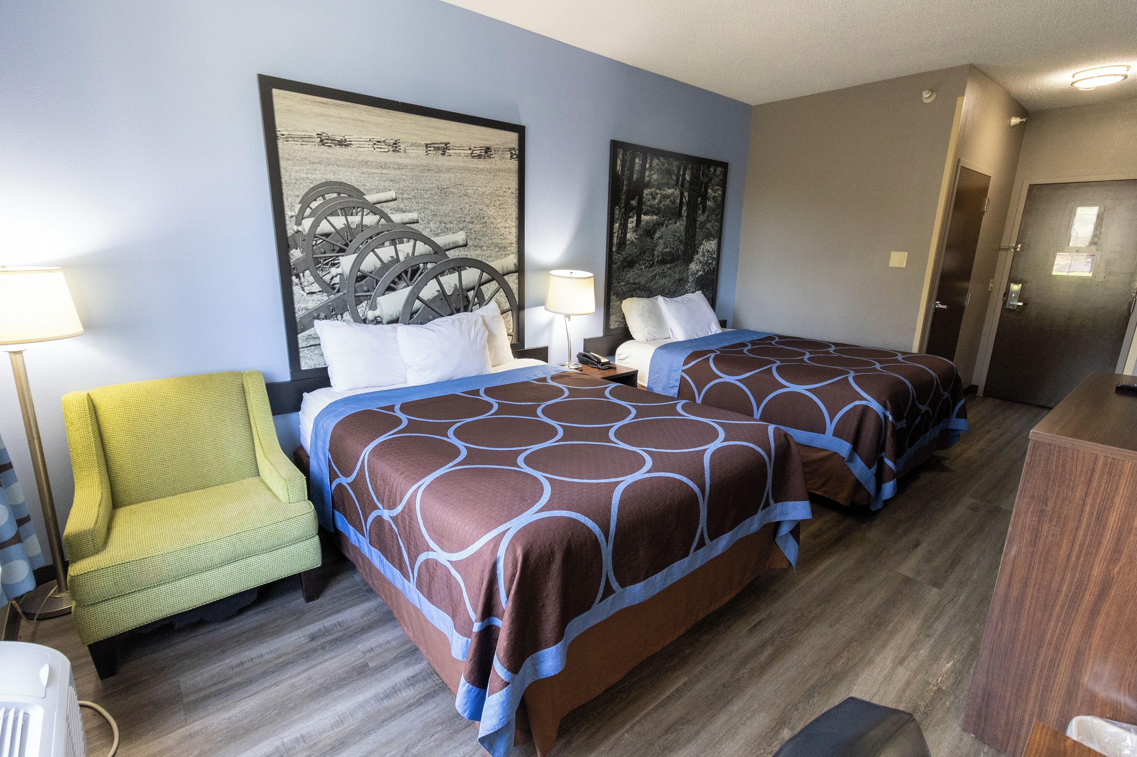 Une chambre d’hôtel avec deux lits, une chaise et des œuvres d’art accrochées aux murs.