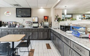 Una cocina moderna con televisor de pantalla plana, cafeteras, una estación de servicio para hacer panqueques y un cartel de desayuno.