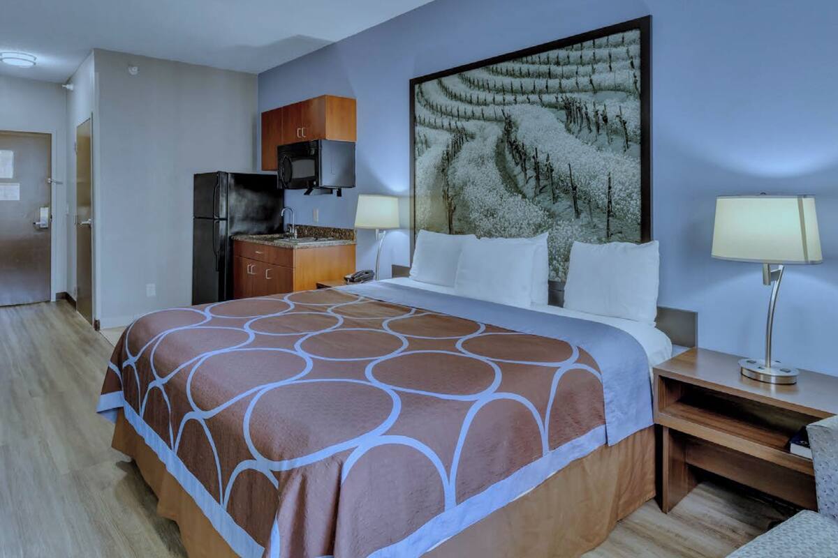 Habitación de hotel con una cama grande, un televisor de pantalla plana, un refrigerador, un escritorio de madera y un cuadro en la pared.