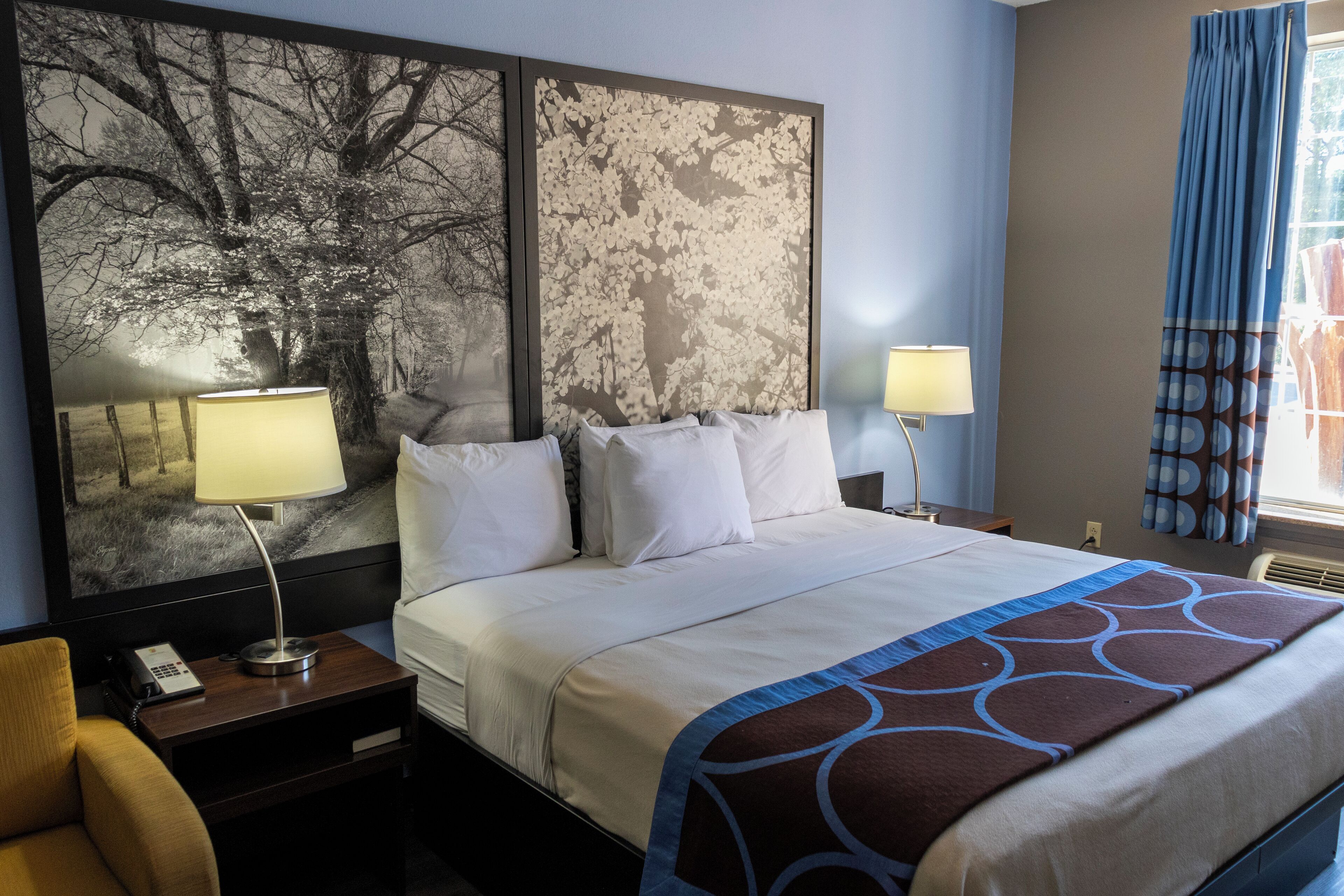 A hotel room with a large bed, two bedside lamps, a nightstand with a phone, and a chair.