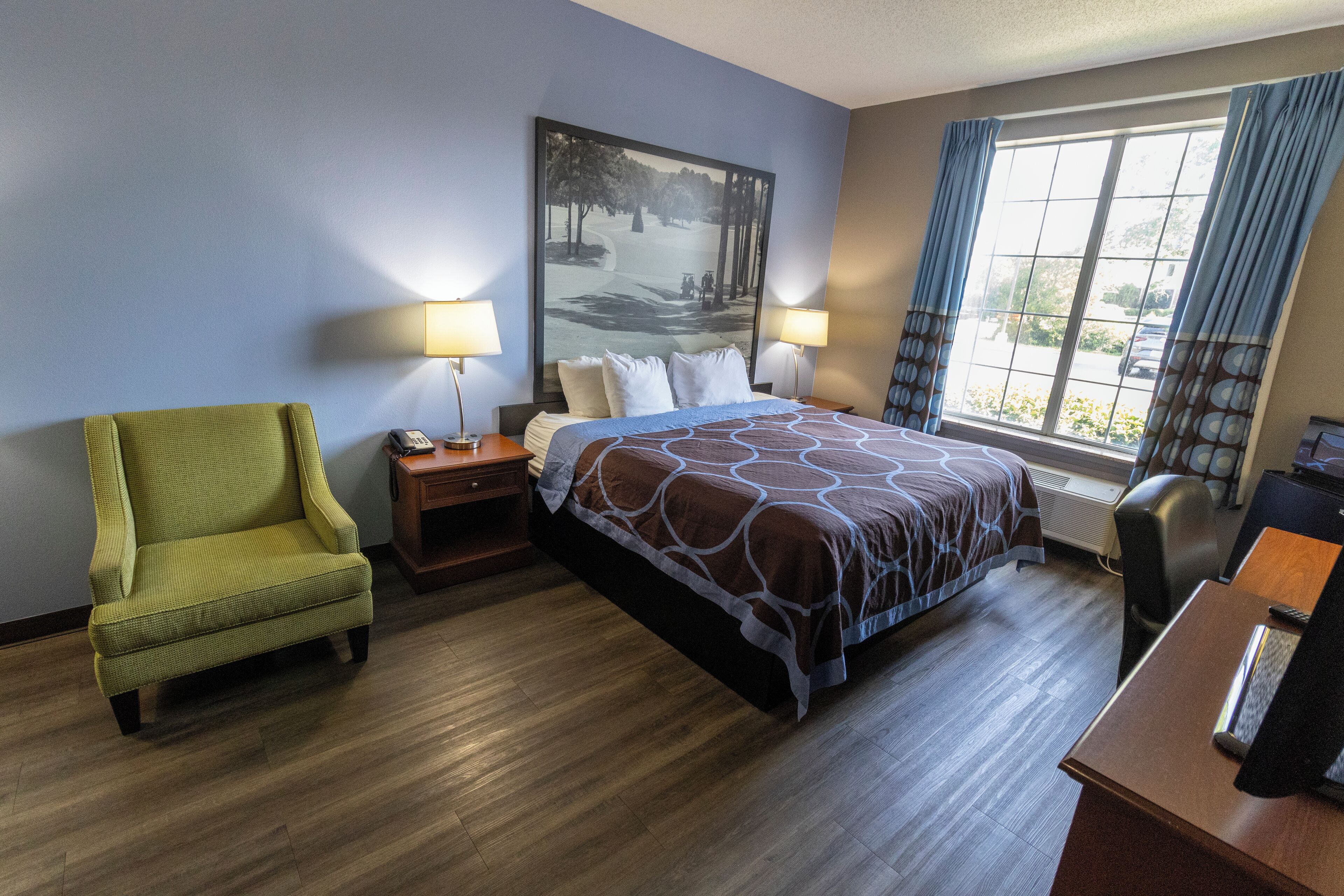 Habitación de hotel con cama, una silla, escritorio y ventana con cortinas.
