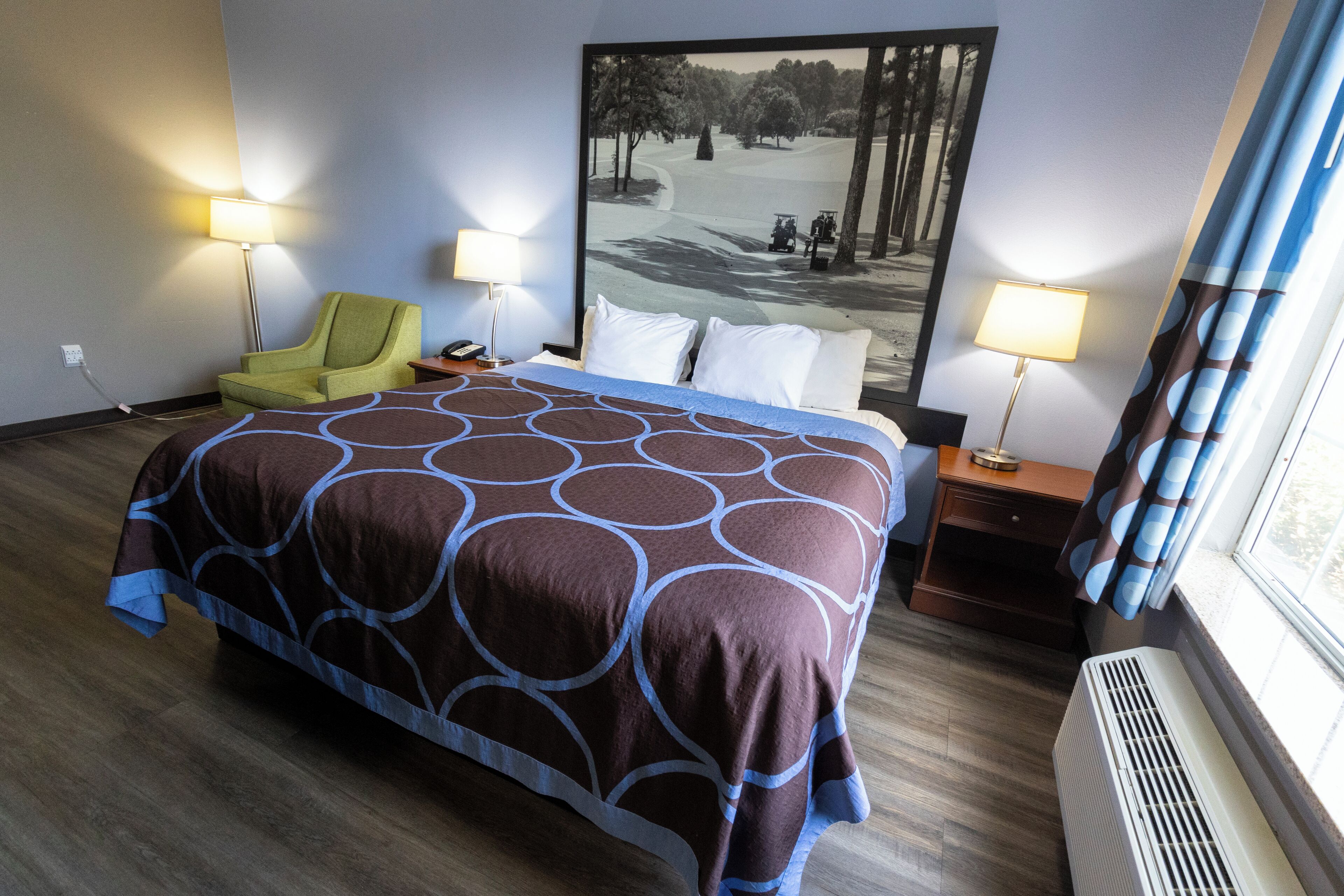 Une chambre d’hôtel avec un grand lit, deux lampes de chevet, une chaise, une fenêtre avec des rideaux et un climatiseur fixé au mur.