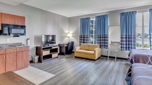 Una habitación de hotel con kitchenette, sofá, cama y televisor.