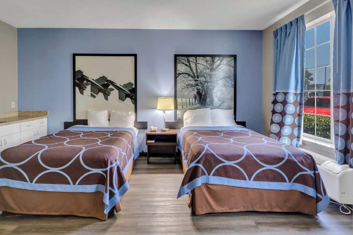 Habitación de hotel con dos camas, una mesita de noche, una lámpara y obras de arte en las paredes.