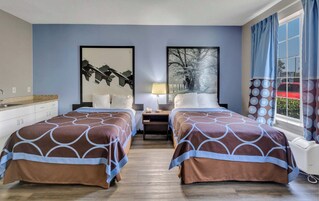 Habitación de hotel con dos camas, una mesita de noche, una lámpara y obras de arte en las paredes.