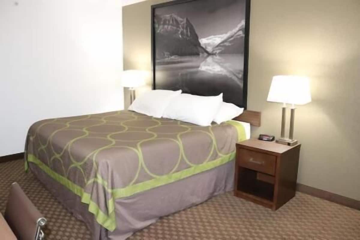 Una camera d'albergo con un letto, due lampade da comodino, un comodino e un quadro incorniciato di grandi dimensioni sulla parete.