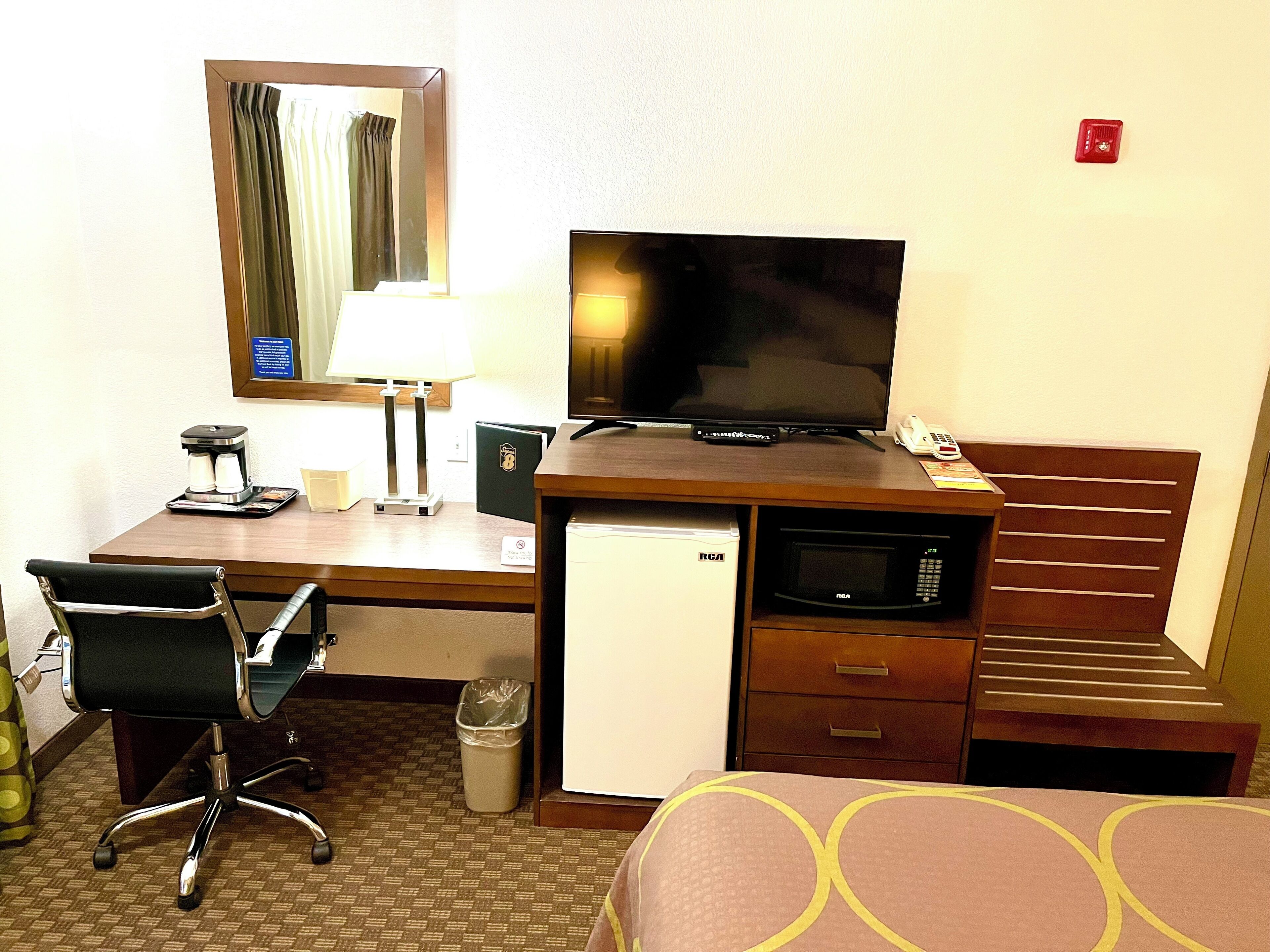 Une chambre d’hôtel équipée d’un bureau, d’une télévision, d’un four à micro-ondes, d’un mini-réfrigérateur, d’une chaise, d’un lit et d’une poubelle.