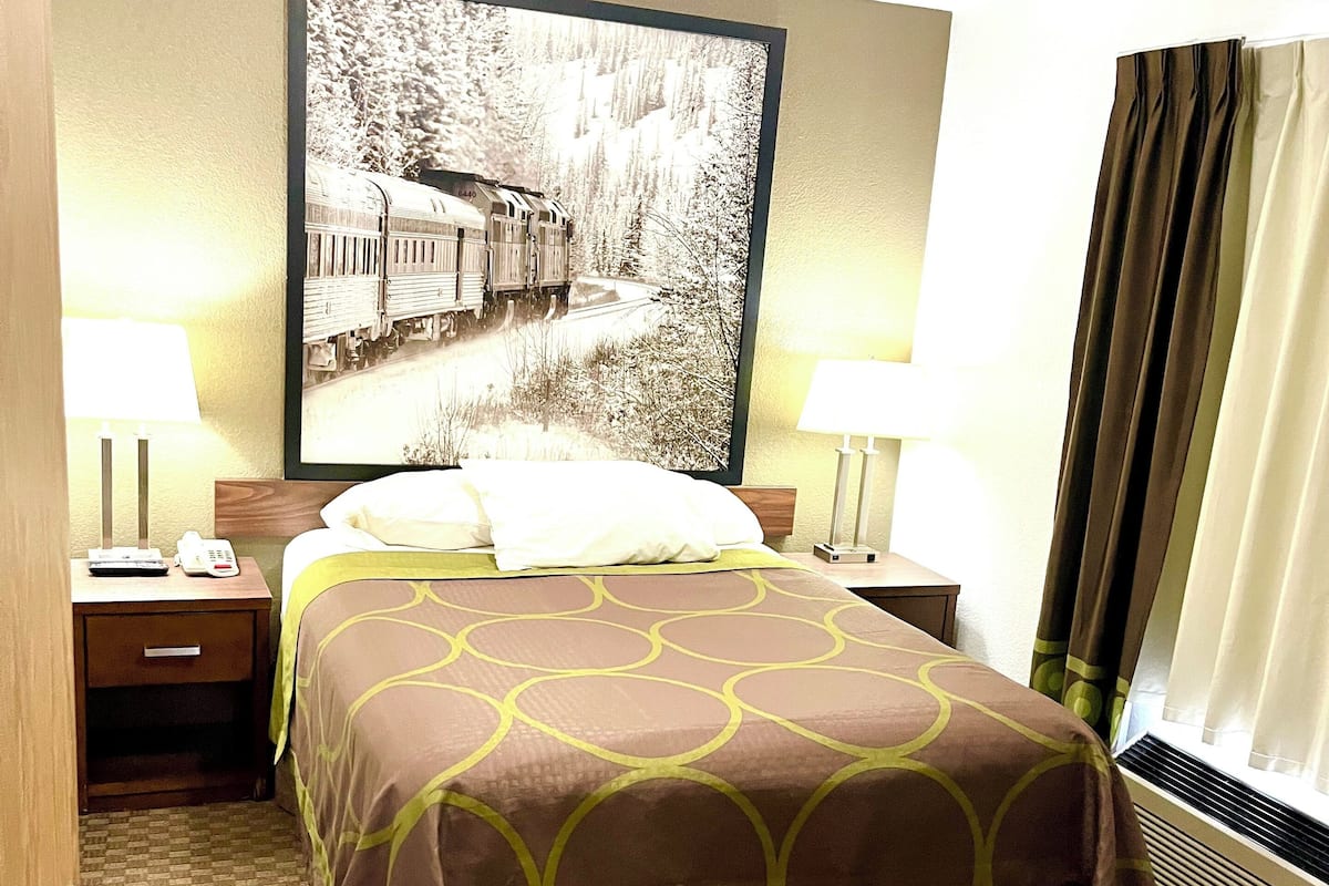 Una camera d'albergo con un letto, due comodini, un quadro appeso e una finestra con tende.