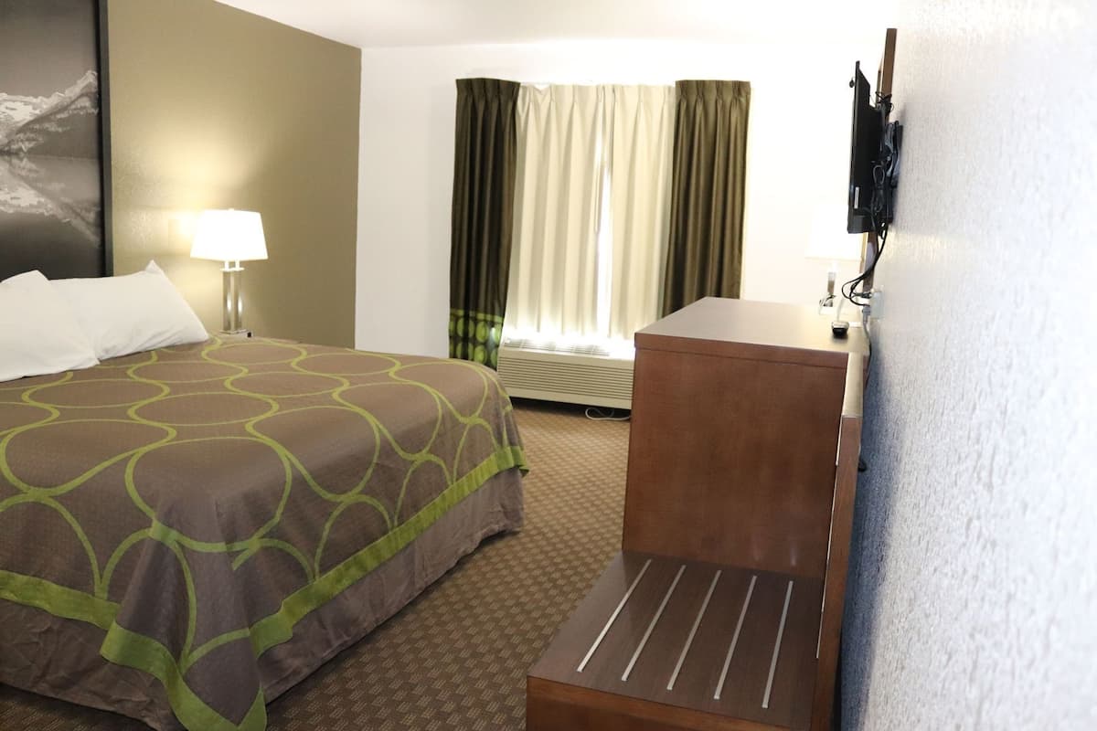Una camera d'albergo con un letto, una scrivania, una sedia, una lampada e una finestra con tende.