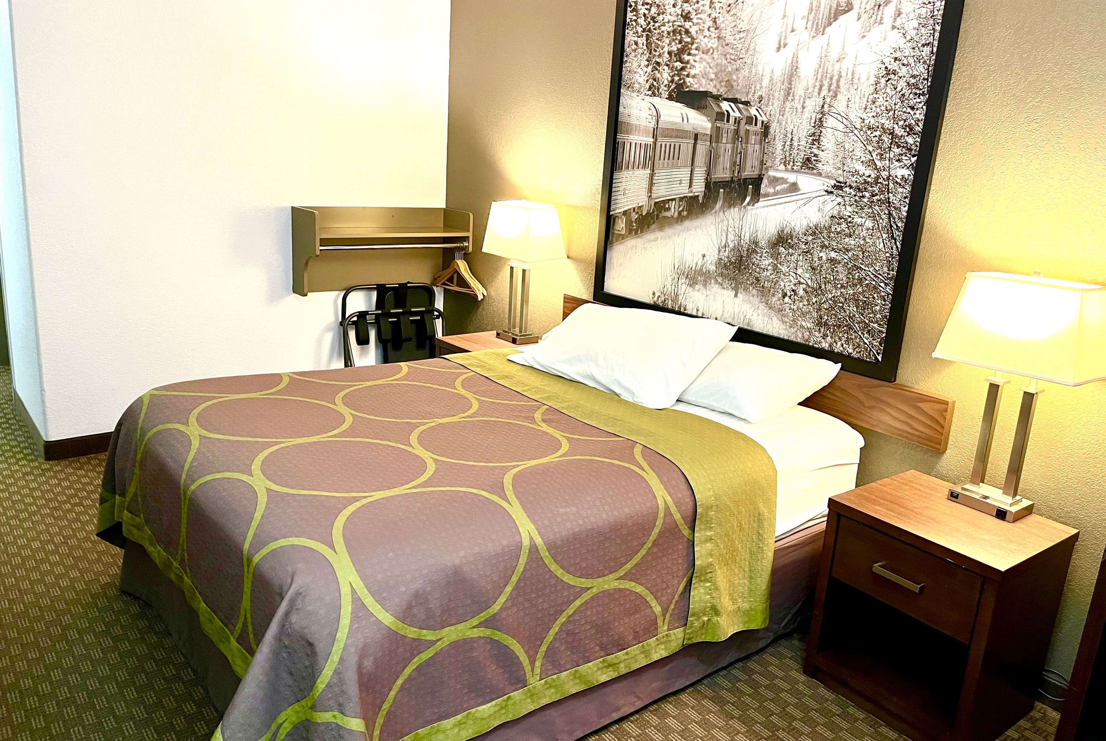 A hotel room with a bed, a nightstand, a lamp, and a wall-mounted picture.