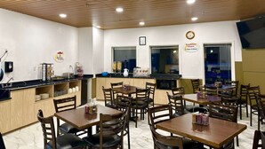 A breakfast area with wooden tables and chairs, a kitchen counter, and a clock indicating breakfast hours. - Super 8 by Wyndham Hinton (Hinton)