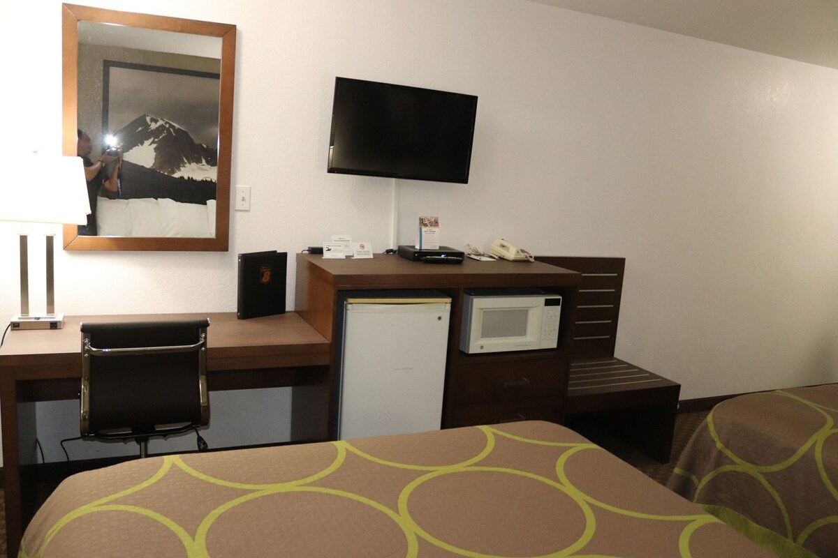 A hotel room with a desk, a television, a refrigerator, a microwave, and two beds with patterned bedding.