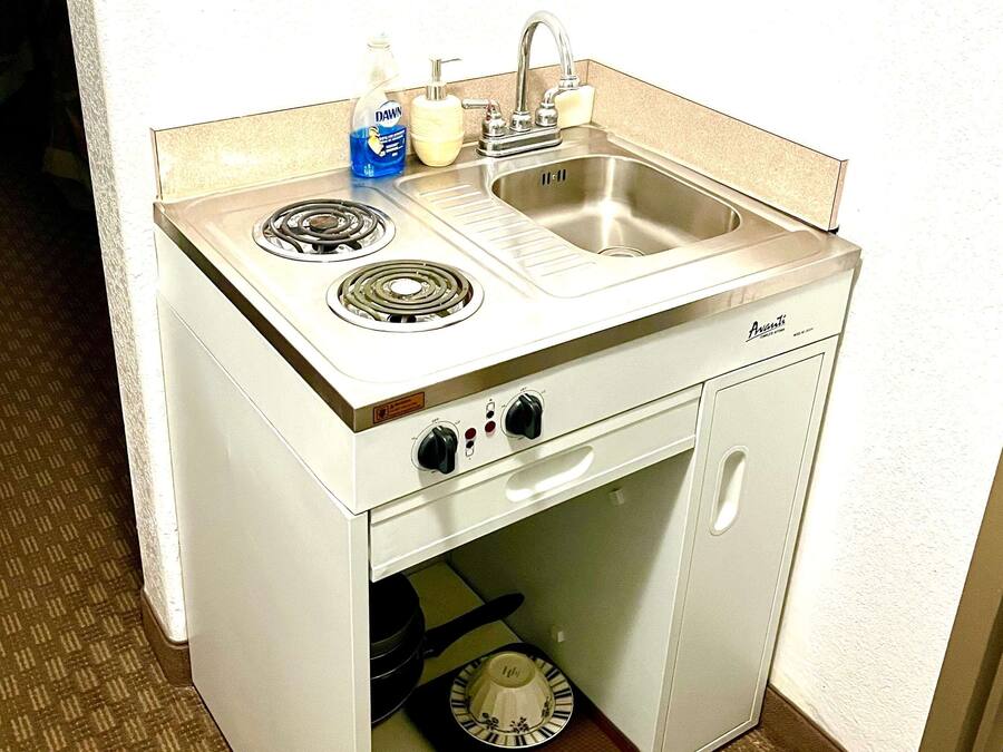 A compact kitchenette with a stove, sink, and storage cabinet.