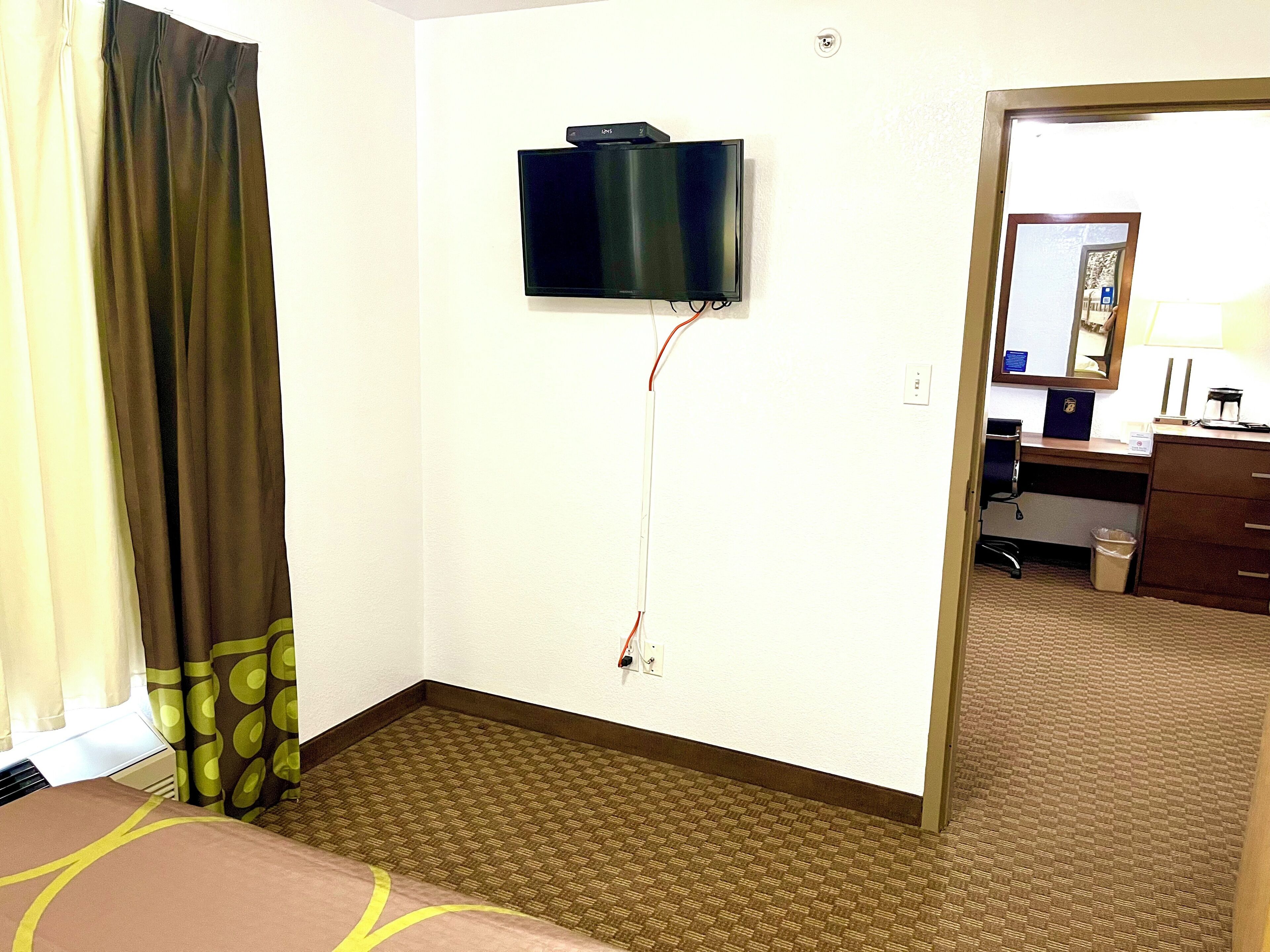 Une chambre d’hôtel équipée d’un téléviseur à écran plat fixé au mur, d’un bureau avec une chaise et d’une petite poubelle.