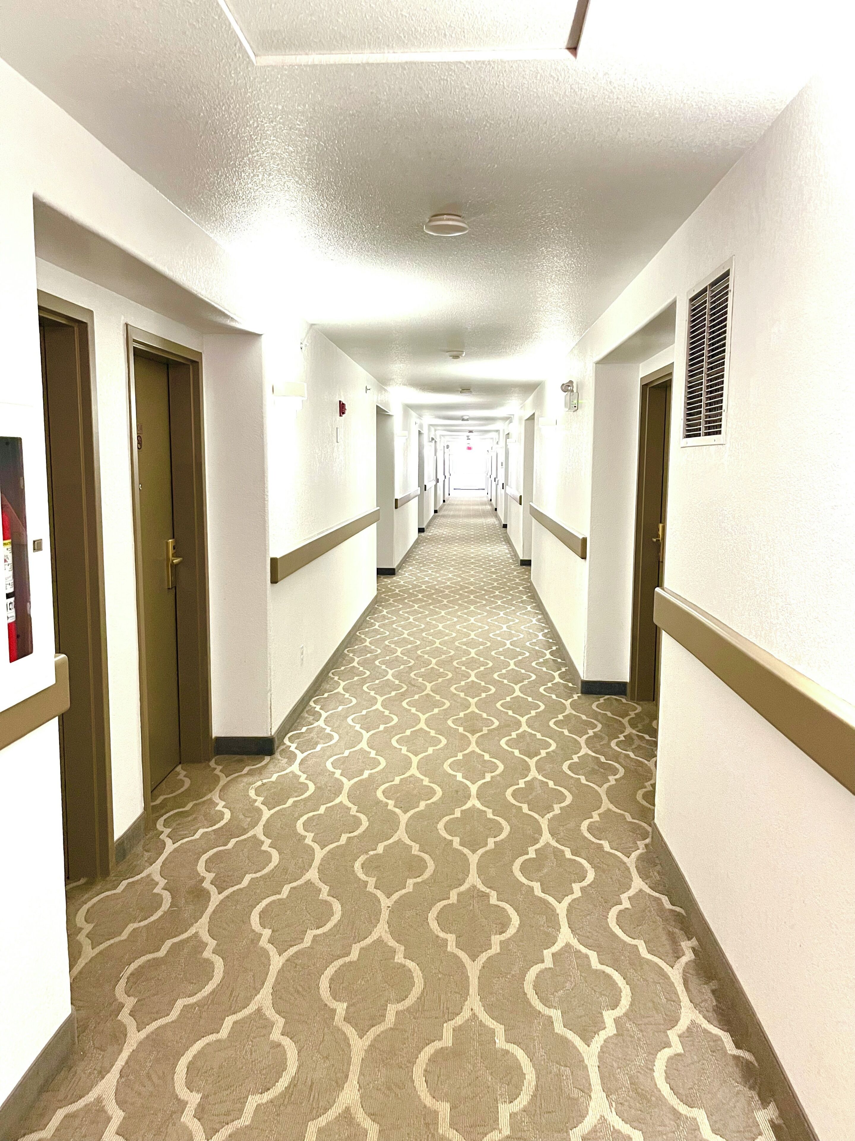 Een hotelgang met een kamerbreed tapijt, witte muren en deuren aan beide kanten.