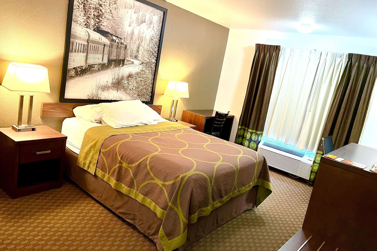 Camera d'hotel con un letto, due comodini, un tavolino da notte, un'ampia finestra con tende e un condizionatore d'aria a parete.