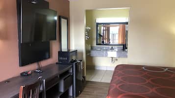 Habitación de hotel con una cama, un escritorio con silla, televisor, microondas y lavamanos con espejo.