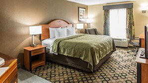A hotel room with a bed, two bedside tables with lamps, a desk with a chair, and a window with curtains. - Quality Inn & Suites Columbus West - Hilliard (Columbus)