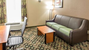 A hotel room with a sofa, a wooden table, a chair, a patterned carpet, and a window with curtains. - Quality Inn & Suites Columbus West - Hilliard (Columbus)