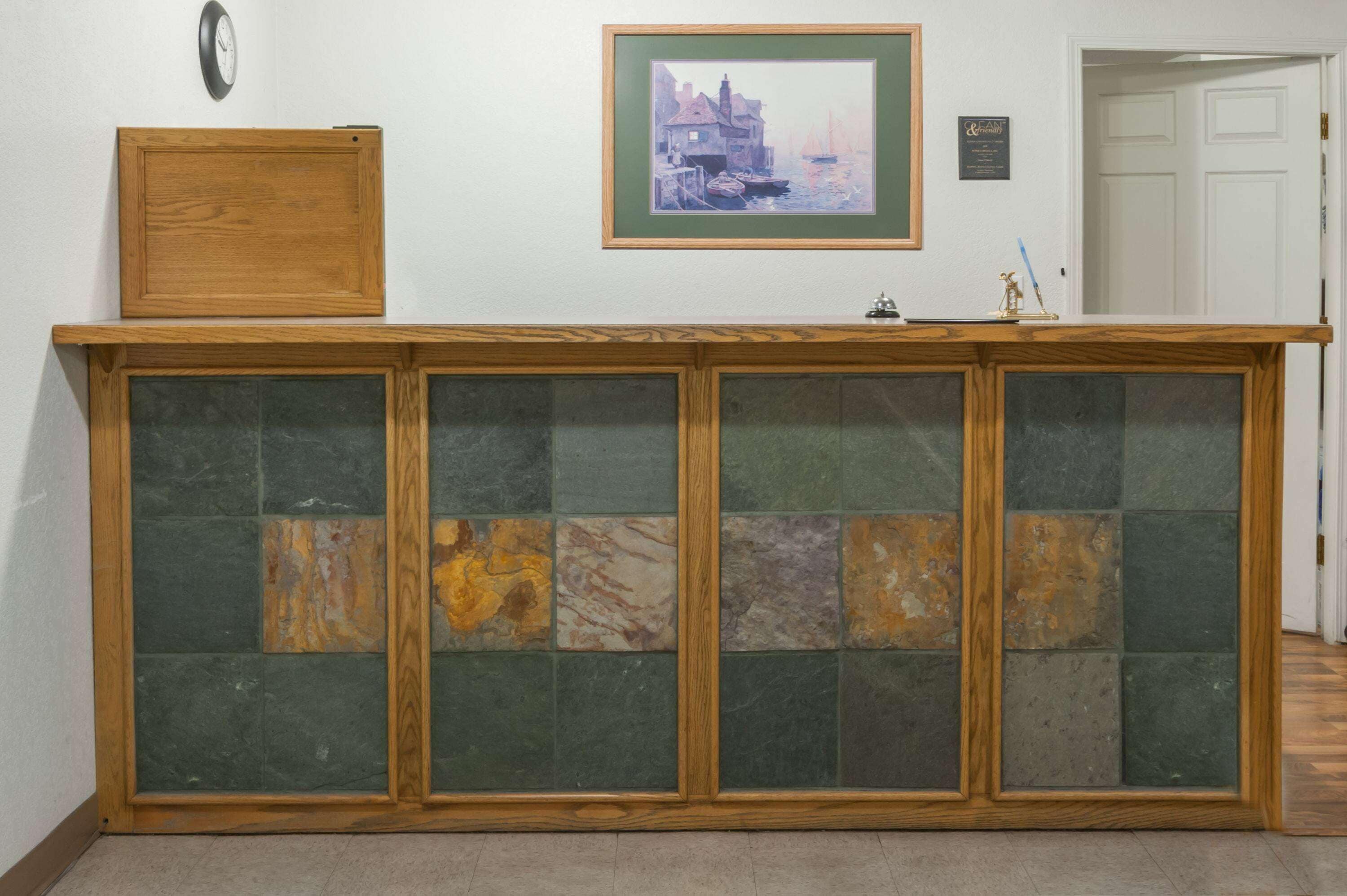 Un mostrador de recepción con estructura de madera, un reloj y un cuadro en la pared.