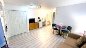 A living room with a sofa, a TV, a coffee machine, and a dining table with chairs.