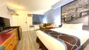 A hotel room with a bed, a TV, a dresser, a sofa, and a large window with curtains.