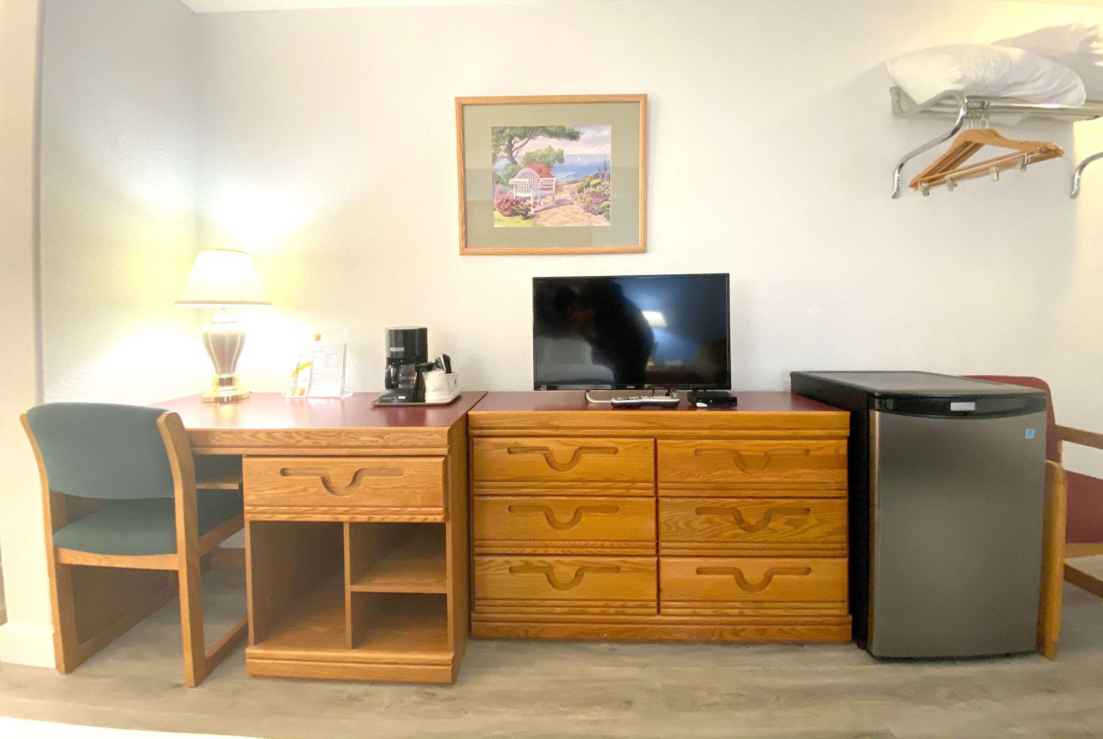A compact hotel room with a wooden desk, a television, a refrigerator, and a chair.