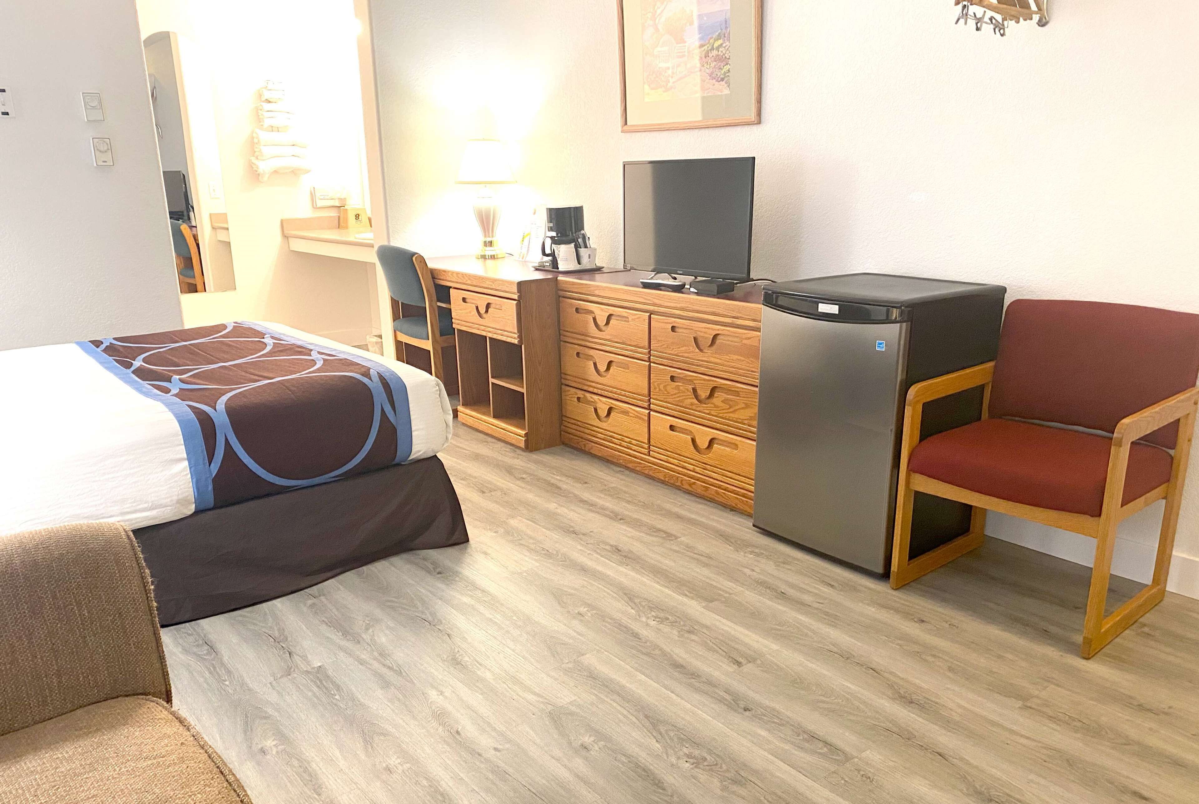 Une chambre d’hôtel comprenant un lit, un bureau avec un ordinateur et un réfrigérateur, ainsi qu’une chaise.