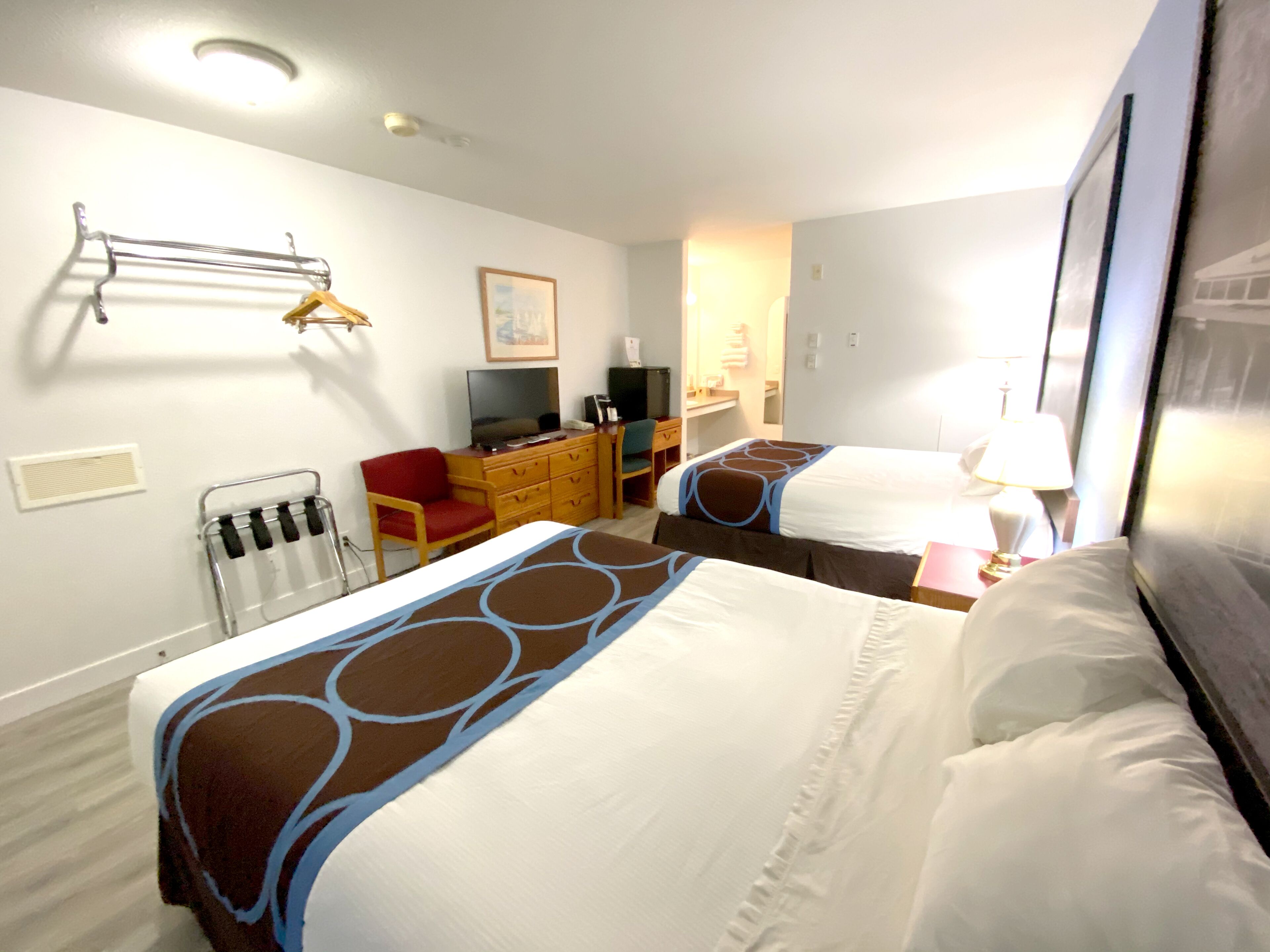 A hotel room with two beds, a desk, a chair, a television, and a radiator.