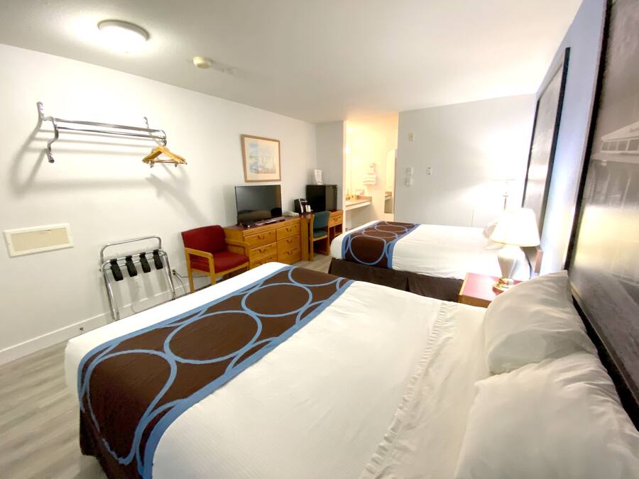 A hotel room with two beds, a desk, a chair, a television, and a radiator.