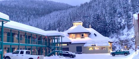 A hotel with a snow-covered exterior, a visible restaurant, and a parking area with vehicles.