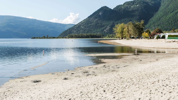 A beach with a clear view of the lake, mountains in the background, and a row of buildings along the shore.