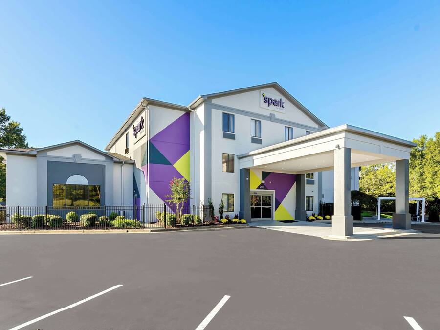 Un hotel moderno con una fachada geométrica llamativa, un acceso cubierto y un estacionamiento.