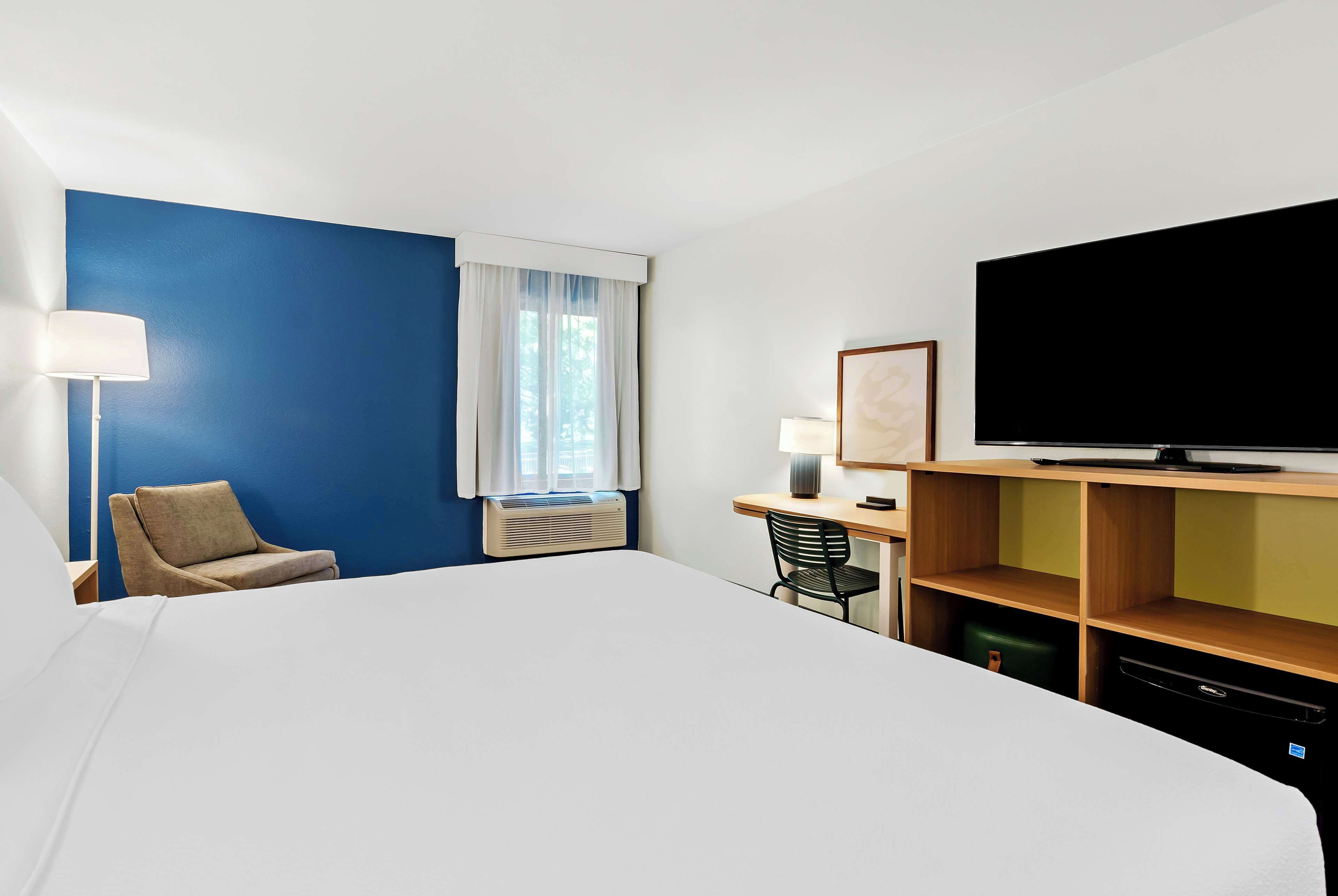 Una habitación de hotel con una cama grande, un escritorio con una silla, un televisor y una ventana con cortinas.