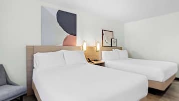 A hotel room with two beds, a desk, and a chair. There is a painting on the wall and a framed picture above the desk.