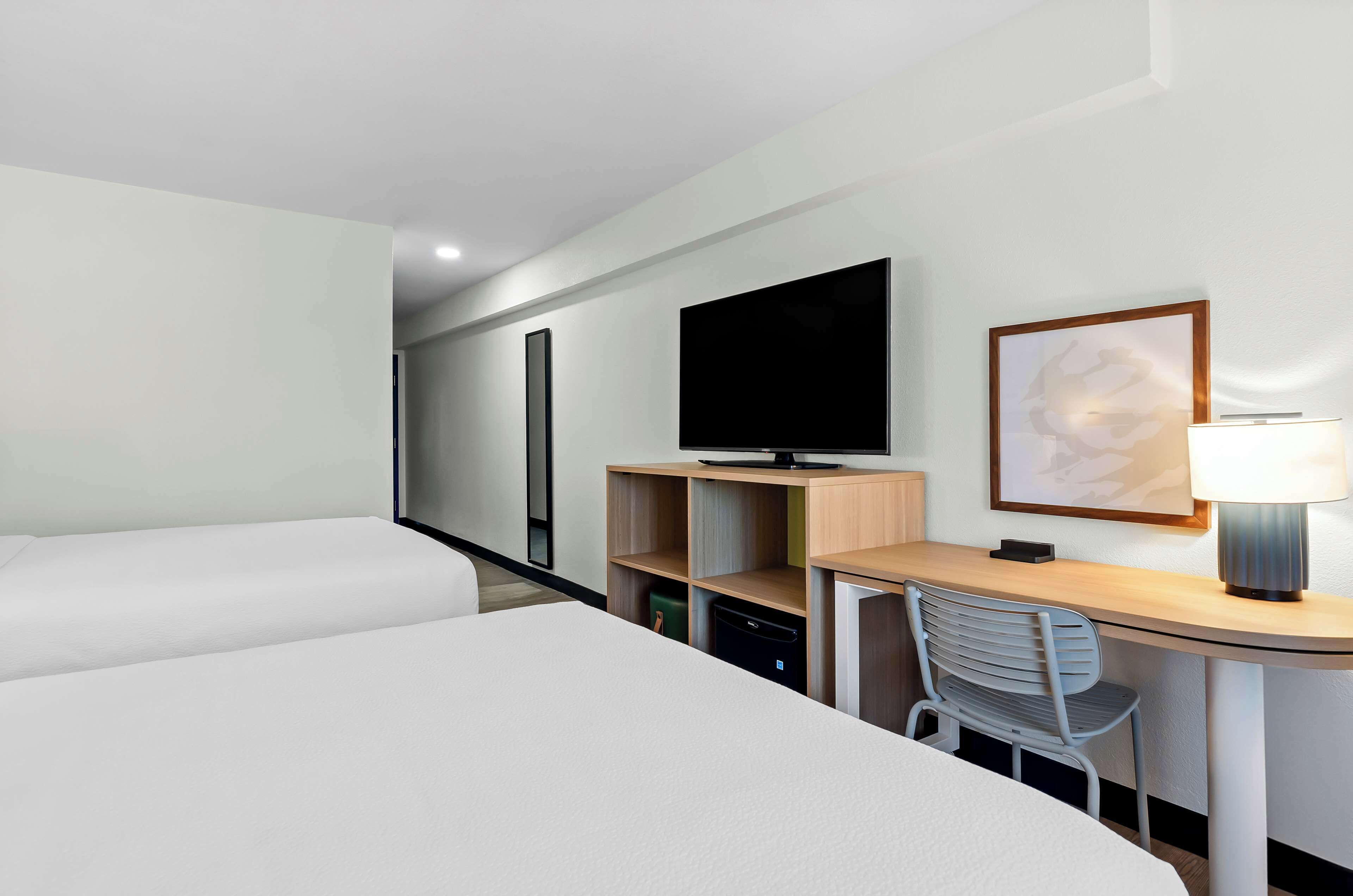 A hotel room with a bed, a desk with a chair, a television, and a lamp.