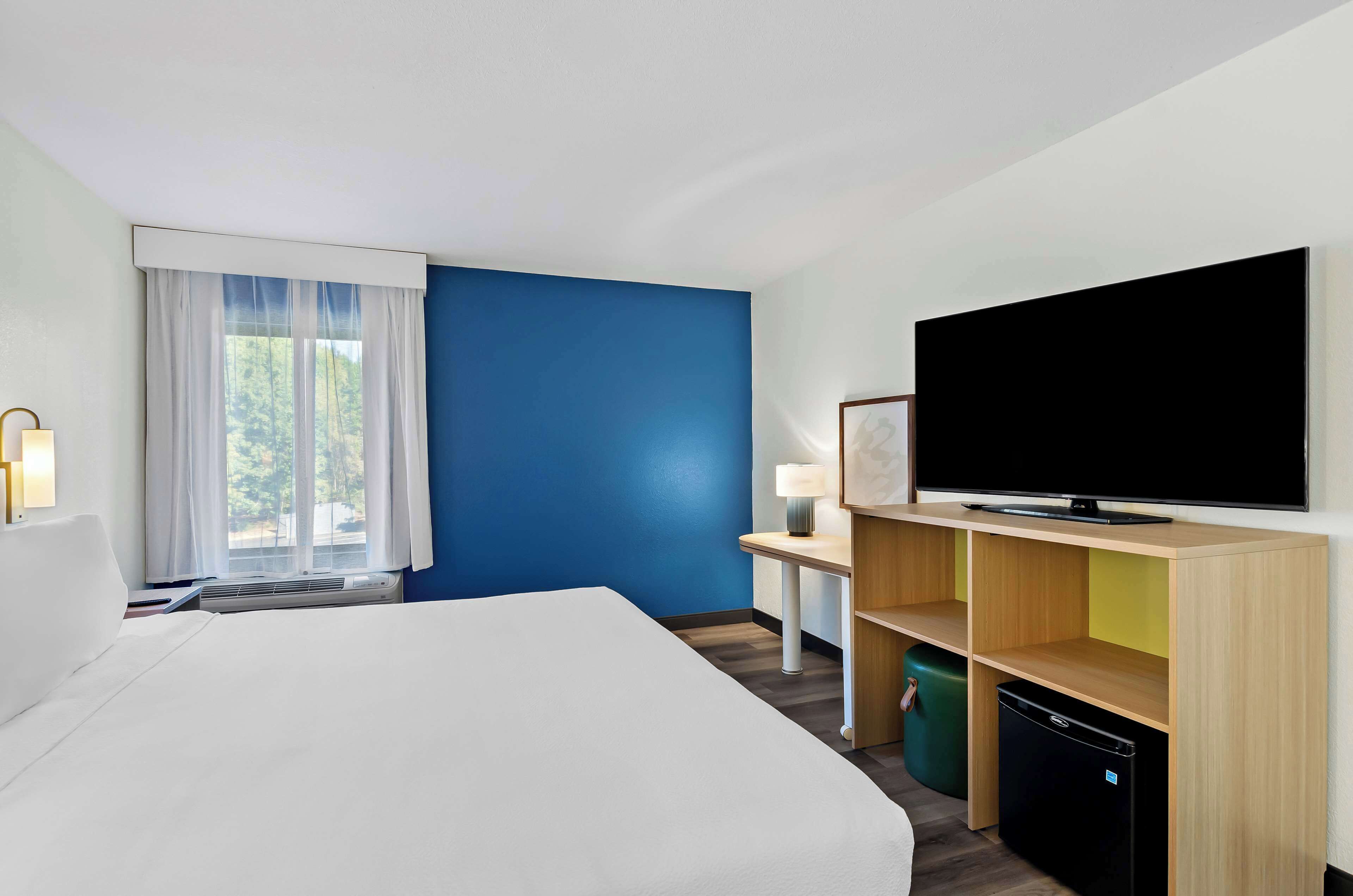 Una habitación de hotel con una cama, televisor, escritorio con lámpara y un refrigerador pequeño.