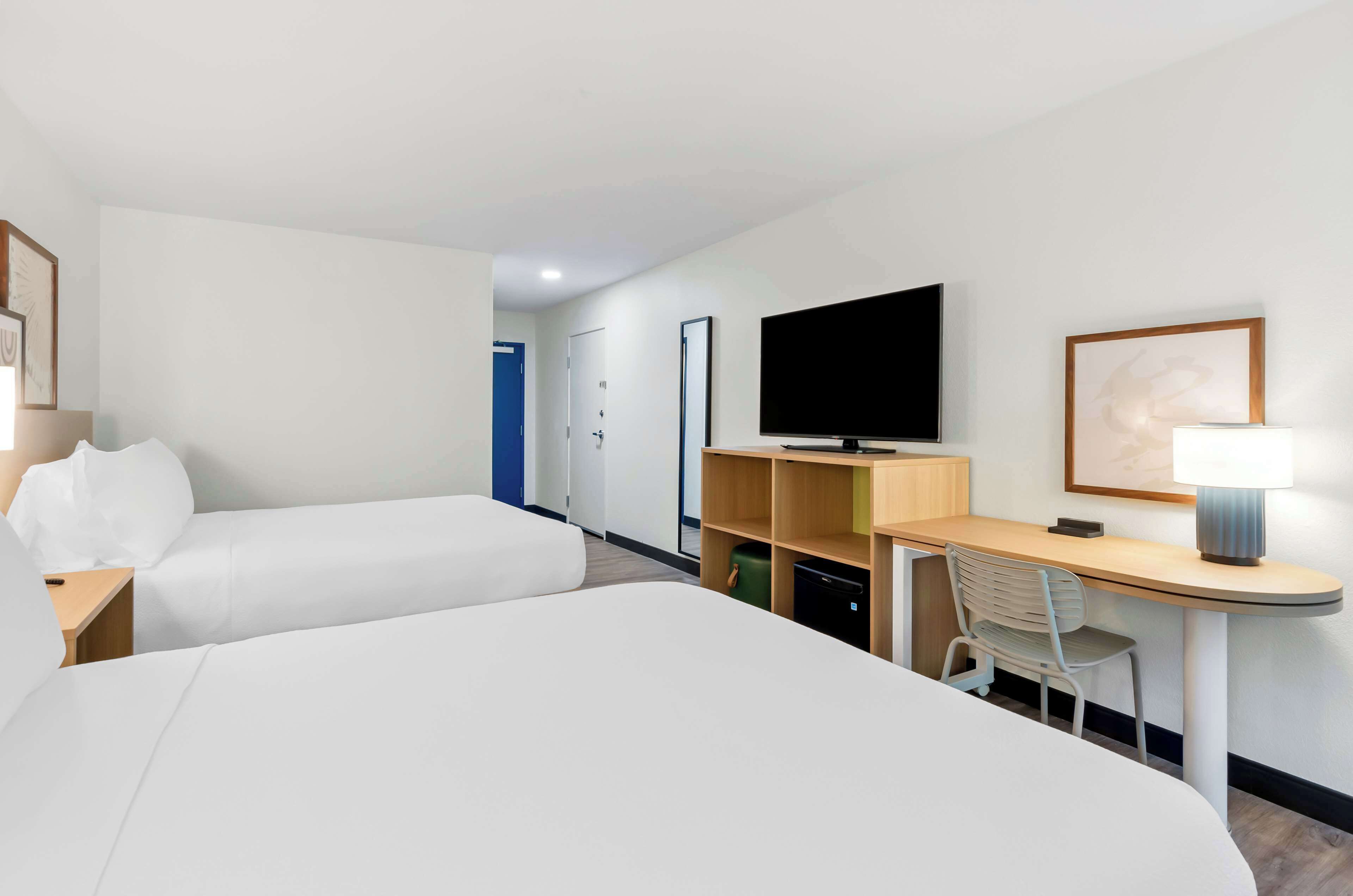 Una camera d'albergo con un letto, una scrivania, una sedia, una televisione e una lampada.