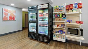 A hotel lobby with two beverage refrigerators stocked with various drinks, a microwave on a shelf, and snack dispensers. - Spark by Hilton Winston-Salem University (Winston-Salem)