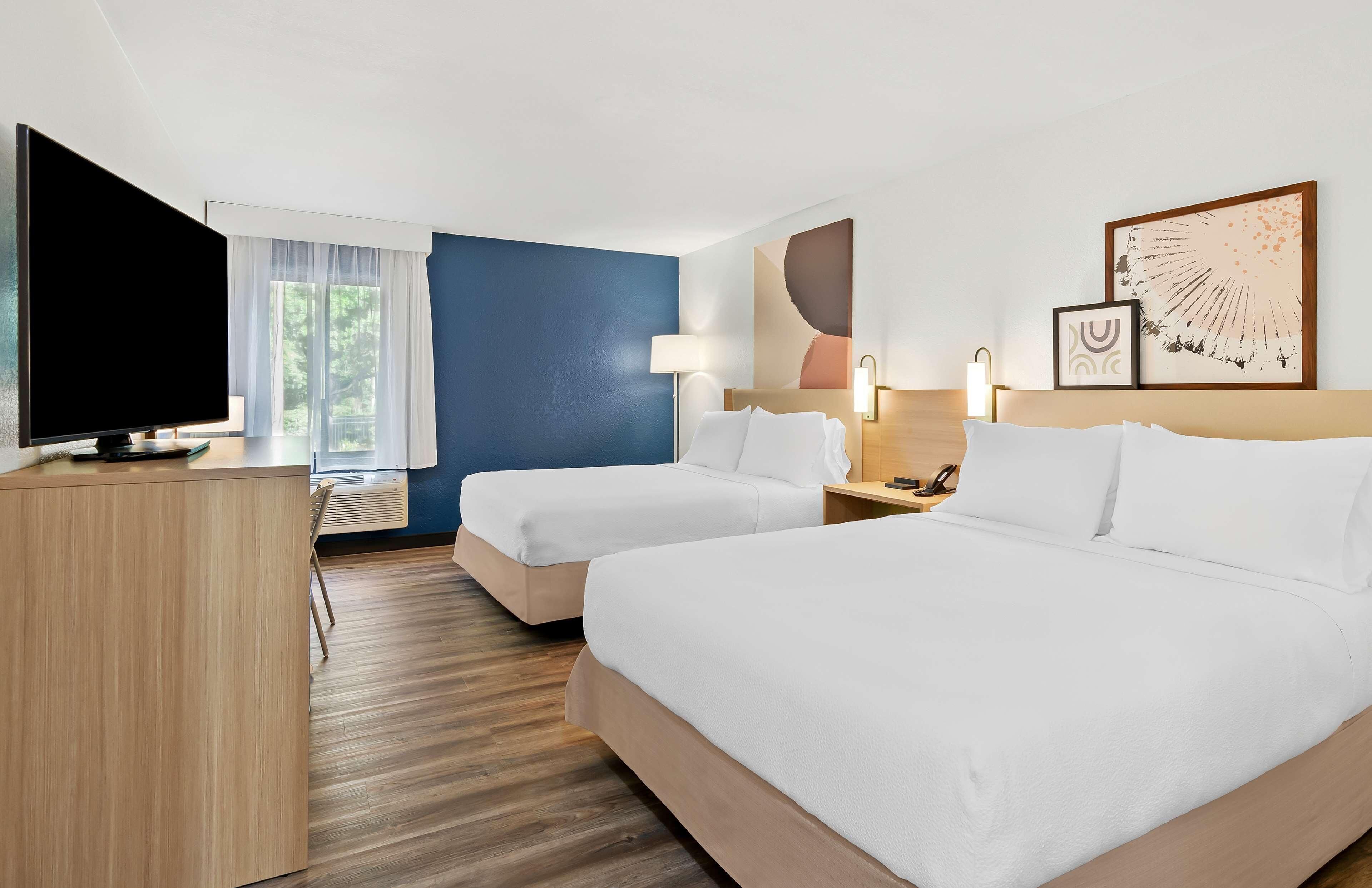 A hotel room with two beds, a desk, a TV, and artwork on the walls.