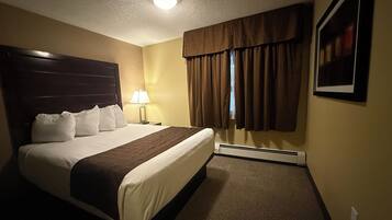 A hotel room with a large bed, a nightstand, a lamp, a window with curtains, and a framed picture on the wall.