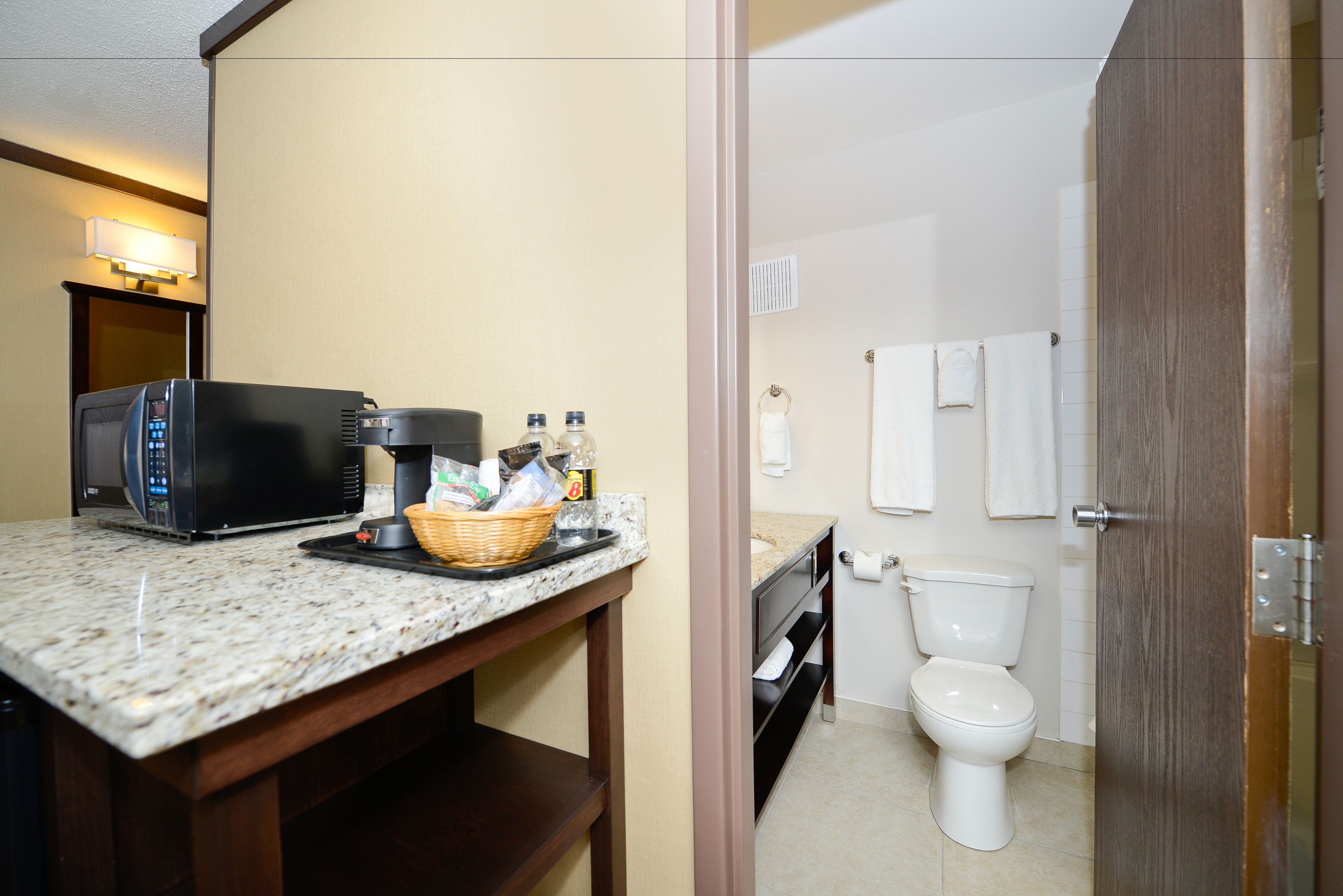 A bathroom with a toilet, a sink, a mirror, and a microwave on a countertop.