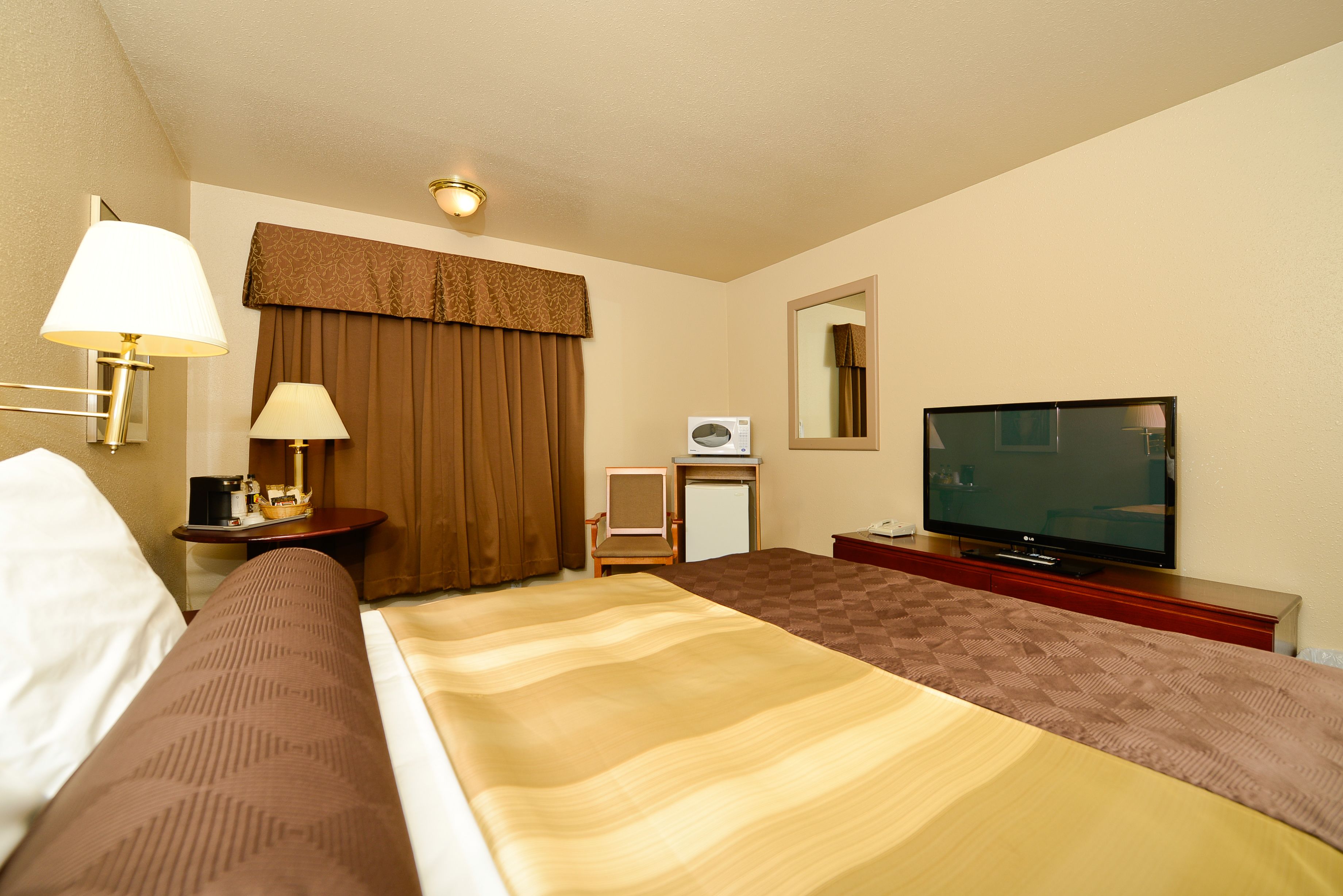 A hotel room with a bed, a television, a desk with a lamp, a chair, and a small refrigerator.