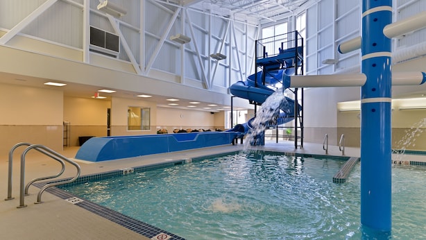 An indoor swimming pool with a water slide, a lifeguard stand, and a blue and white color scheme. - Siding 16 Lodge (Wetaskiwin)
