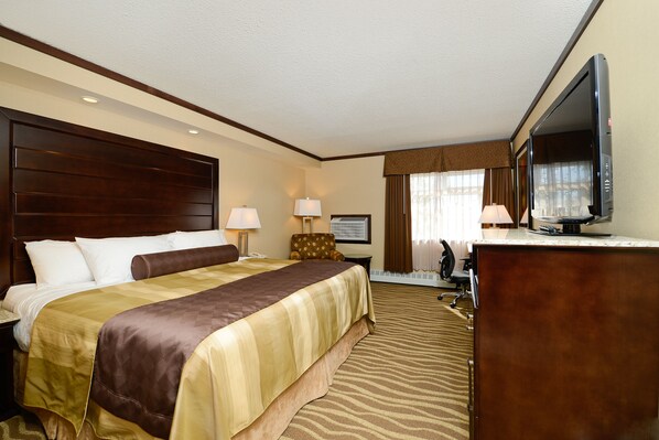 A hotel room with a large bed, a desk, a television, and a chair.