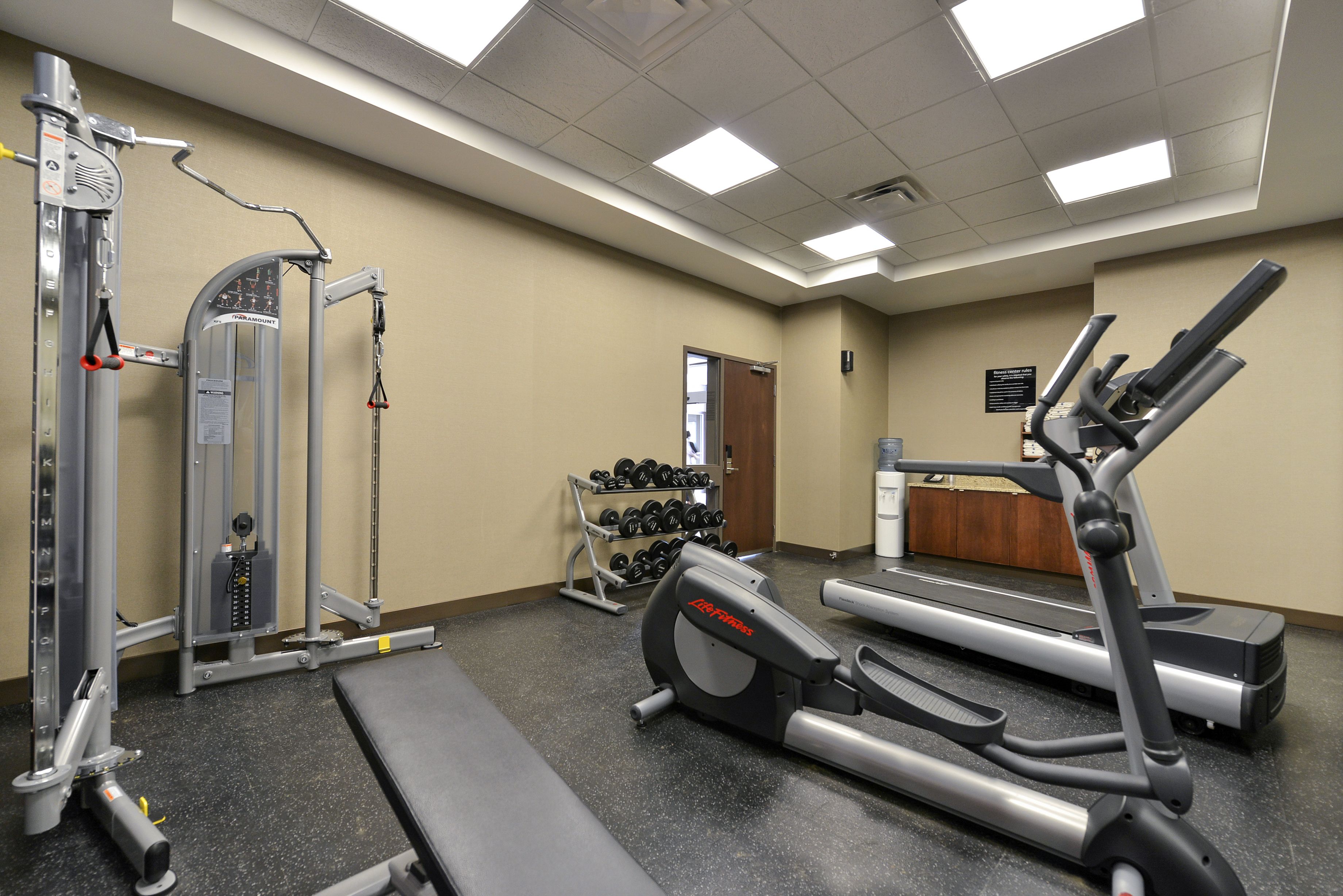 A gym with cardio machines, weightlifting equipment, and a bench.