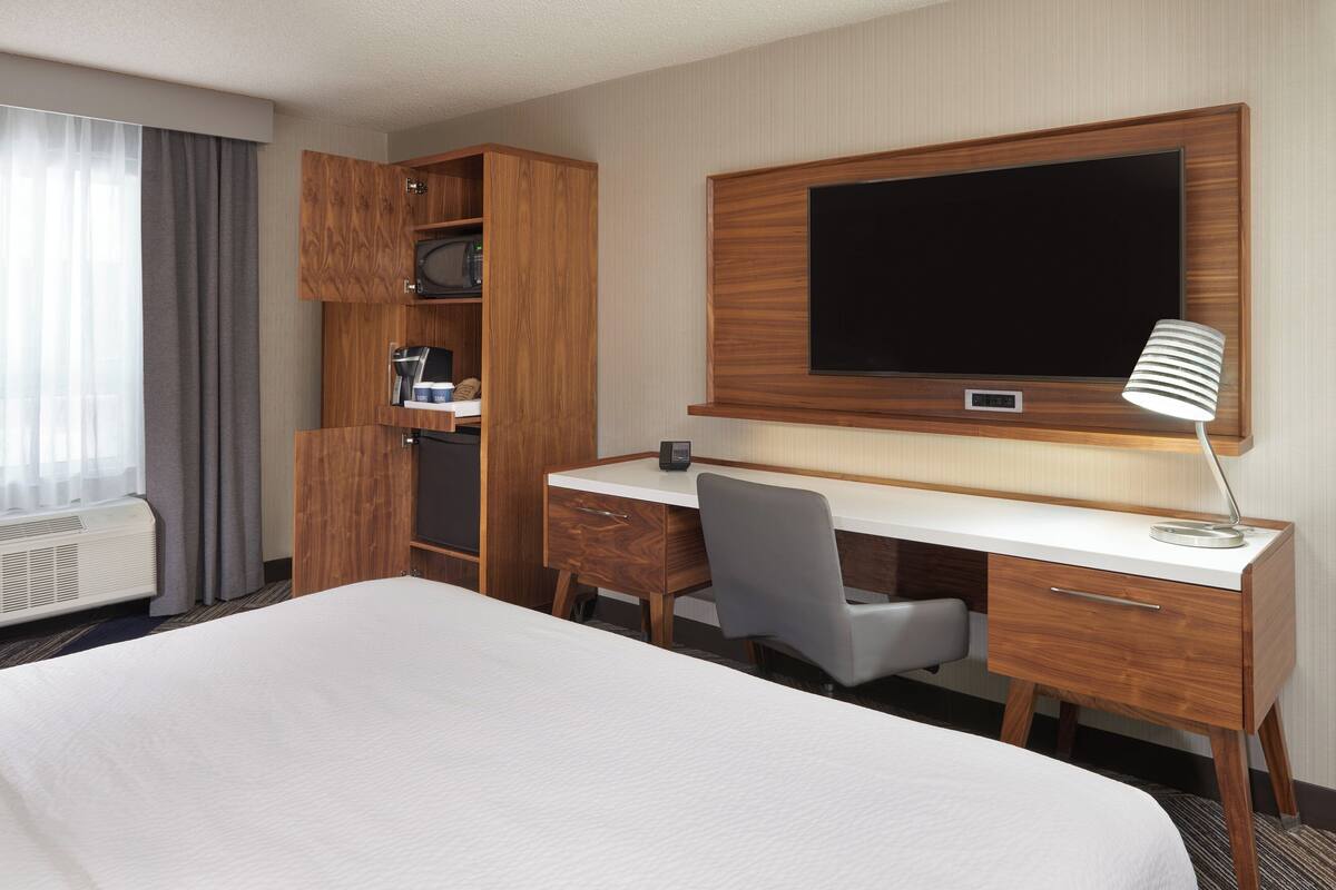 A hotel room with a large bed, a wooden desk, a television, and a desk lamp.